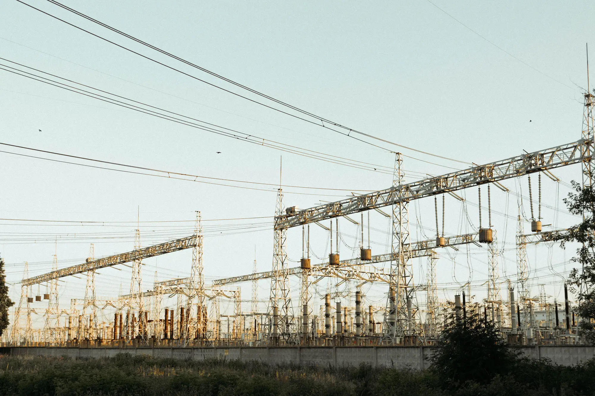 Lattice gantries and busbars of an outdoor high-voltage switchyard against a pale evening sky